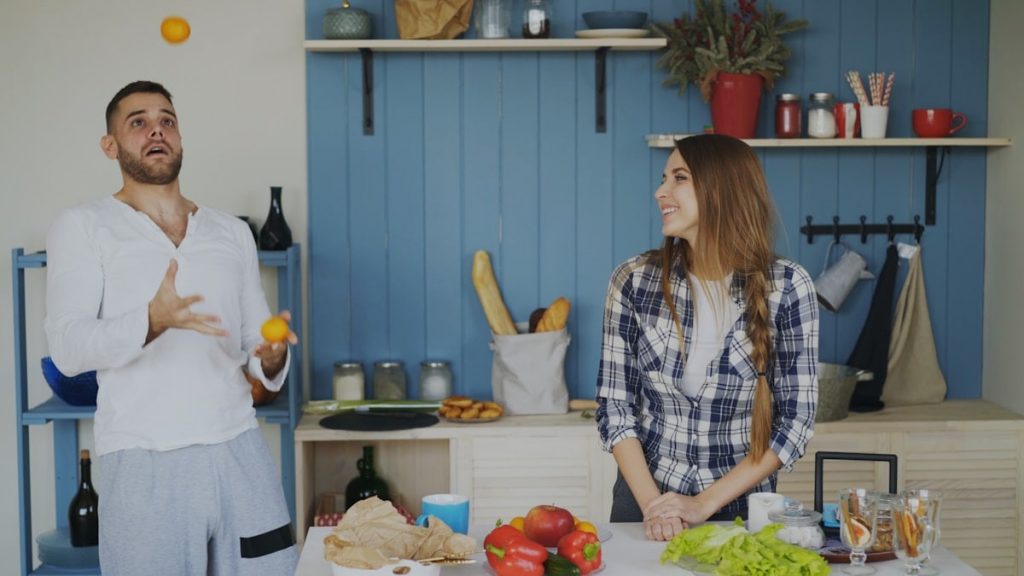 Attractive loving couple having fun in the kitchen. Handsome man juggle with fruits to impress his girlfriend at home